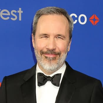 A man with a beard, wearing a tuxedo with a bow tie, smiles in front of a blue backdrop featuring the text 'silvercrest' and a logo. The setting appears elegant, suggesting a formal event.