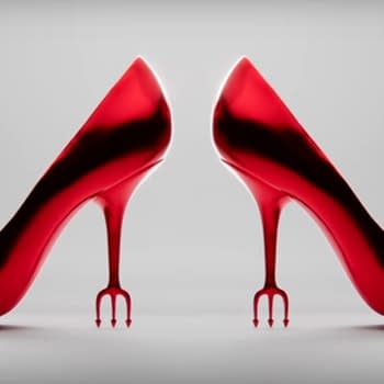 A pair of glossy red high-heeled shoes with unique fork-like heels, highlighted against a neutral backdrop. The design evokes a sense of fashion-forward sophistication and edginess.