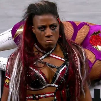 Athena, a professional wrestler, stands in focus displaying a fierce expression, with long multicolored hair and a striking outfit embellished with red and silver accents. In the background, another wrestler in a purple outfit, Thunder Rosa, is visible as the pair compete for championship gold at ROH Supercard of Honor.