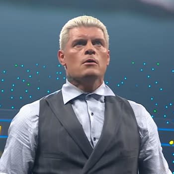 Cody Rhodes looks visibly upset during a contract signing, wearing a formal outfit with a vest and button-up shirt. The background features colorful lights, indicative of a wrestling event atmosphere.