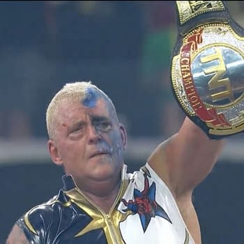 Dustin Rhodes, wearing a star-themed outfit and with blue face paint, celebrates triumphantly as he raises the TNT Championship belt high above his head after winning at AEW All In: Texas.