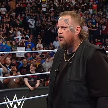 Jelly Roll, a global entertainment superstar, stands in the WWE SmackDown ring with a serious expression, surrounded by an excited crowd holding signs and taking photos.