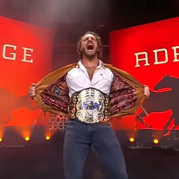 Wrestler Hangman Adam Page proudly displays his newly won AEW Championship while standing on stage, holding his jacket open to display the belt. The dual screens behind page feature bright red lights and the words 'PAGE' and 'ADAM' along with silhouettes of galloping horses as Page makes his entrance on AEW Dynamite.