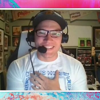 Ian Riccaboni smiles while speaking on the AEW Unrestricted podcast, wearing glasses and a headset, with a collection of framed memorabilia in the background.