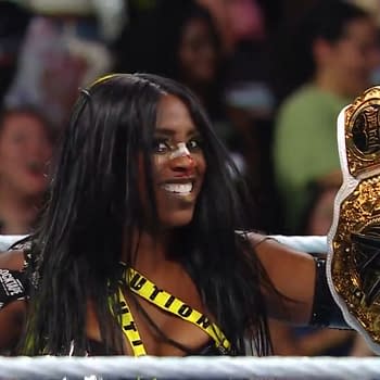 Naomi, with a joyful expression, holds the WWE Women's Championship above her head, showcasing her victory after cashing in at WWE Evolution. She wears a black and yellow outfit with caution tape details, and there is a bandage on her nose.