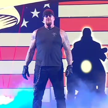 The Undertaker stands in a wrestling ring, wearing a sleeveless black shirt, black gloves, and sunglasses, with a dramatic red, white, and blue backdrop. A mist surrounds him, enhancing the theatrical atmosphere.