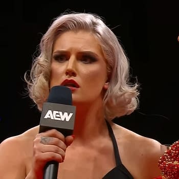 A female wrestler, Toni Storm, is holding a microphone and has an intense expression as she confronts another wrestler, Mercedes Moné, during a segment on AEW Dynamite. The scene captures a moment of heightened tension ahead of their upcoming match.