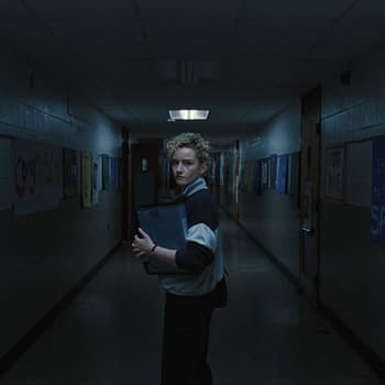 A student stands in a dimly lit school hallway, holding a binder, with various campaign posters on the walls advocating for different student candidates. The atmosphere conveys a sense of tension and anticipation.