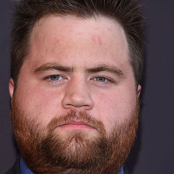 Actor Paul Walter Hauser with a beard and close-cropped hair, poses against a dark background at the "Kingdom" Season 2.5 Premiere in Los Angeles.