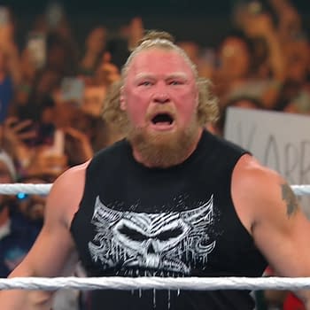 Brock Lesnar stands in the wrestling ring, passionately shouting with intense expression. He is wearing a black tank top adorned with a graphic design, surrounded by enthusiastic fans in the background holding up signs and taking photos.