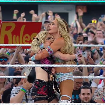 Charlotte Flair and Alexa Bliss embrace in celebration after winning the tag team title at WWE SummerSlam. A cheering crowd is visible in the background, holding signs and phones.