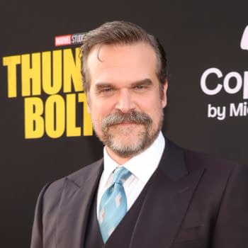 David Harbour smiles at the premiere of 'Thunderbolts,' dressed in a dark suit with a light blue tie, set against a black backdrop featuring the movie title.