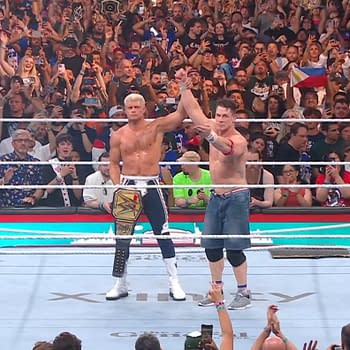 In a wrestling ring, John Cena raises Cody Rhodes' arm in victory after Rhodes defeats him for the WWE title at SummerSlam, while a cheering crowd watches in the background.