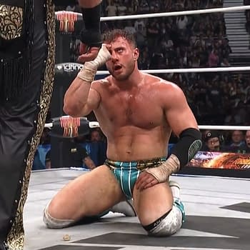 In the wrestling ring at the AEW x NJPW Forbidden Door event, MJF taunts Hangman Adam Page, who is kneeling on the mat with an expression of frustration. The crowd is visible in the background, adding to the atmosphere of the match.
