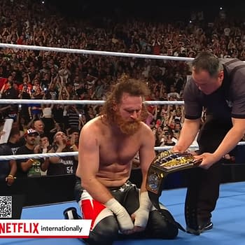 Sami Zayn kneels on the wrestling mat in celebration as a referee presents him with the WWE United States Championship after defeating Solo Sikoa in front of a roaring crowd in France.