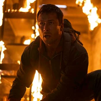 Glen Powell appears as a character in a scene from the Paramount Pictures film "The Running Man," with flames and smoke in the background, conveying a dramatic and intense moment.
