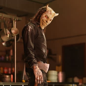 Ethan Hawke portrays The Grabber in Black Phone 2, wearing a menacing mask and holding an axe, set in a dimly lit kitchen environment.