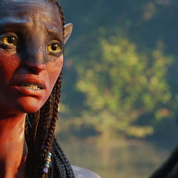A character named Neytiri, portrayed by Zoe Saldaña in 20th Century Studios' 'AVATAR: FIRE AND ASH', is depicted with intricate facial markings and braided hair, expressing a strong emotion against a lush backdrop.