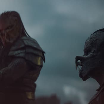 A scene from the film 'Predator: Badlands' features two alien characters, Kwei and Dek, dressed in armor. Kwei holds a glowing sword, while Dek observes amidst a dramatic cloudy background.