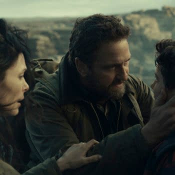 A dramatic scene from the film 'Greenland 2: Migration,' featuring three characters: a woman with long dark hair, a man with a beard, and a young boy. The man is holding the boy's face, expressing emotion, while the woman looks concerned in the background.
