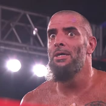 A close-up of Mark Briscoe with an astonished expression while engaged in a scene on AEW Collision, surrounded by bright stage lights.