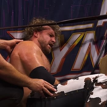 Referees tend to a hurt wrestler, Hangman Adam Page, seated near the ring after a brutal match. The scene captures the intensity of wrestling with visible injuries and concern from the officials.