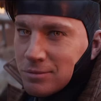 Channing Tatum is depicted in a cinematic scene, wearing a dark headpiece and a brown jacket, with a confident expression as flames flicker in the background.