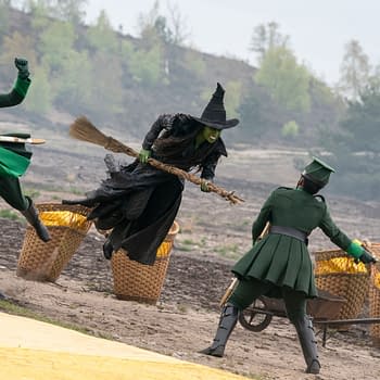 A scene from 'Wicked: For Good' featuring Cynthia Erivo as Elphaba, portrayed in a dramatic pose while flying on her broomstick, wearing a dark dress and a pointed hat. Two characters in green costumes appear to chase her, adding dynamic action to the moment.