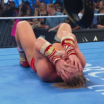 Ilja Dragunov celebrates winning the United States Championship on WWE SmackDown, lying on the mat with his hands over his face in disbelief. The audience is visible in the background, expressing excitement.