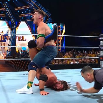 John Cena performs the Walls of Jericho on AJ Styles during a wrestling match at WWE Crown Jewel in Perth. The audience is visible in the background, captivated by the intense action.