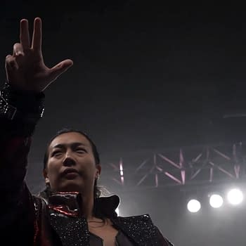 Konosuke Takeshita, dressed in a sparkling outfit, celebrates as the new IWGP Heavyweight Champion, signaling victory with a raised hand gesture in a spotlighted arena.