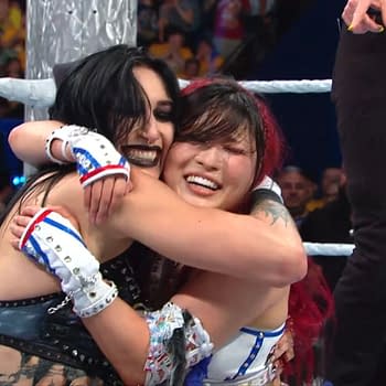 Rhea Ripley and Iyo Sky embrace in a joyful hug after their victory at WWE Crown Jewel in Perth, Australia. Both wrestlers are expressing happy emotions in the celebratory moment.