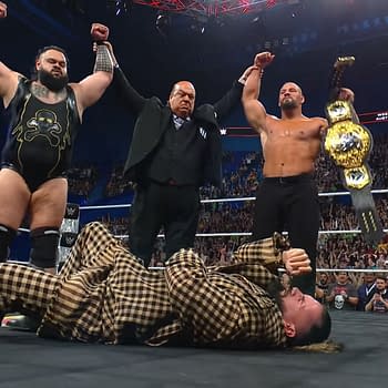 Seth Rollins lies defeated on the mat while his former stable celebrates above him, raising their arms in triumph. The atmosphere is charged with the energy of a WWE event.