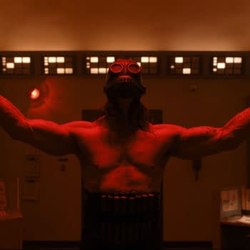 A dramatic scene featuring James Preston Rogers portraying a character called Psycho Killer, with bare arms raised and a gas mask, set in a dimly lit control room adorned with blinking lights.