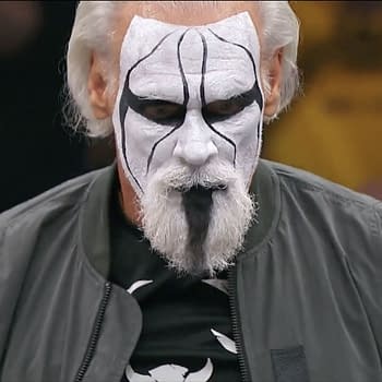 A wrestler known as Sting stands in a ring, wearing dramatic face paint with black and white patterns and a gray jacket. His intense expression captures the energy of the moment.