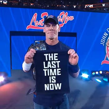 John Cena stands in the center of the wrestling ring at Madison Square Garden, holding a black towel with the words "THE LAST TIME IS NOW" printed in large white letters. He wears a championship belt and a cap, with bright stage lights illuminating the scene.