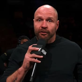 Jon Moxley delivering a promo on AEW Collision, holding a microphone while speaking to the audience. The background includes fans watching attentively.