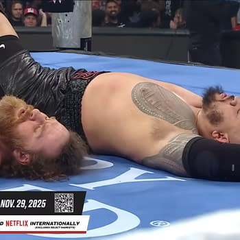 WWE superstars Sami Zayn and Solo Sikoa lie on the wrestling mat, seemingly resting or taking a break during a match. Their expressions reflect exhaustion after a physical encounter.