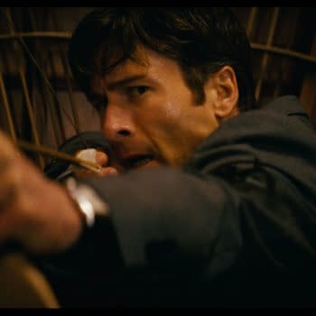 A man in a suit aims an arrow from a bow, displaying intense focus and determination. The background features wooden paneling, adding to the dramatic atmosphere.