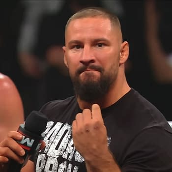 Bron Breakker delivers a powerful promo on WWE Raw, holding a microphone and making a strong gesture with his hand. His focused expression and stance convey the seriousness of his message.