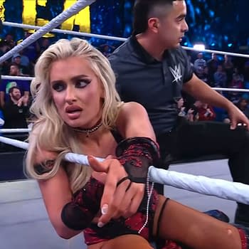 Former NXT Champion Blake Monroe displays a shocked expression while seated on the mat, clutching the ring rope, suggesting a moment of confusion following a title loss in a wrestling match, with a referee nearby and a crowd in the background.