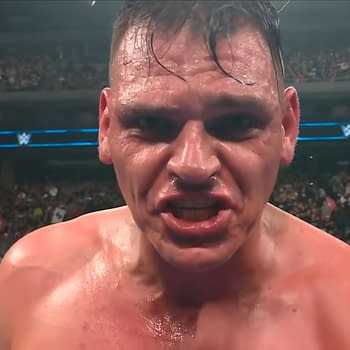 A close-up of Gunther, a wrestler in WWE, appears intense and focused, with sweat on his face and a determined expression. The audience can be seen in the background, creating an energetic atmosphere.