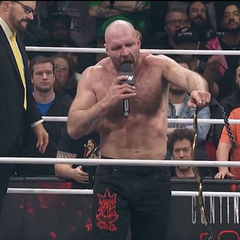 Jon Moxley delivers a passionate promo in the wrestling ring at AEW World's End, holding a championship belt and addressing fans and wrestlers. A commentator stands nearby while the enthusiastic audience is visible in the background.