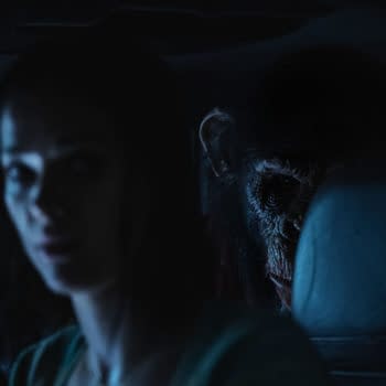 A tense scene from the film 'Primate', featuring Jessica Alexander as Hannah in a dimly lit car, with a menacing chimpanzee lurking in the background, hinting at a suspenseful atmosphere.