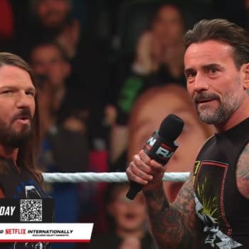 AJ Styles and CM Punk engage in a lively interaction during WWE Raw, with a captivated audience in the background. CM Punk holds a microphone, gesturing as AJ Styles looks on with a focused expression.