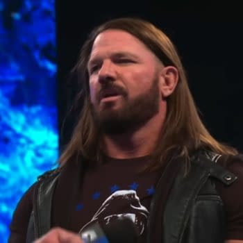 AJ Styles stands on stage during WWE SmackDown, wearing a black vest over a dark t-shirt. The blue backdrop features the WWE SmackDown logo, adding to the energy of the event.