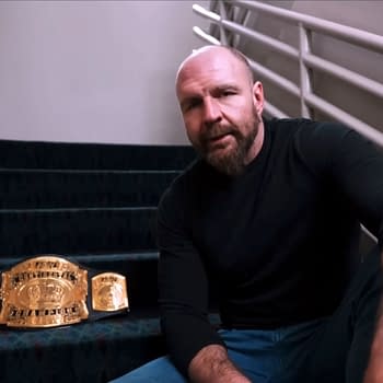 Jon Moxley sitting on stairs backstage, delivering a promo, with a championship belt resting nearby on the steps.