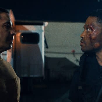 A tense scene from 'Night Patrol' featuring two men facing each other, one dressed in a police uniform and the other in a brown shirt. The officer has visible injuries, including a bruise on his face.