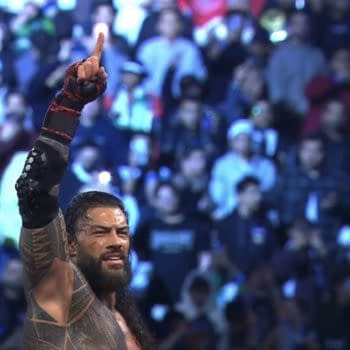 A jubilant Roman Reigns raises his arm in victory after winning the Royal Rumble match, surrounded by a cheering crowd in Saudi Arabia.