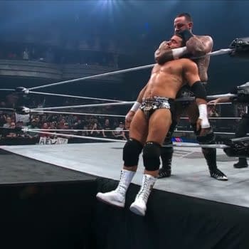 Brody King applies a chokehold to MJF, who is teetering at the edge of the wrestling ring, with referees and spectators visible in the background. The atmosphere is tense and electrifying.